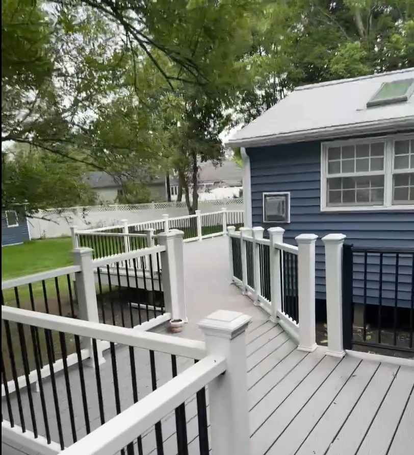 Avant Contracting - Newly built grey composite deck with white railings and black balusters, attached to a blue house.
